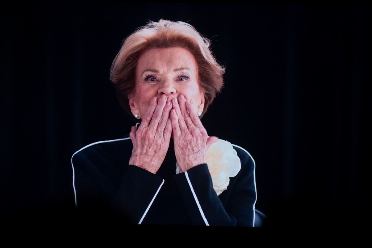 Janette porte ses mains sur ses lèvres en signe de baiser envoyé à son public. 