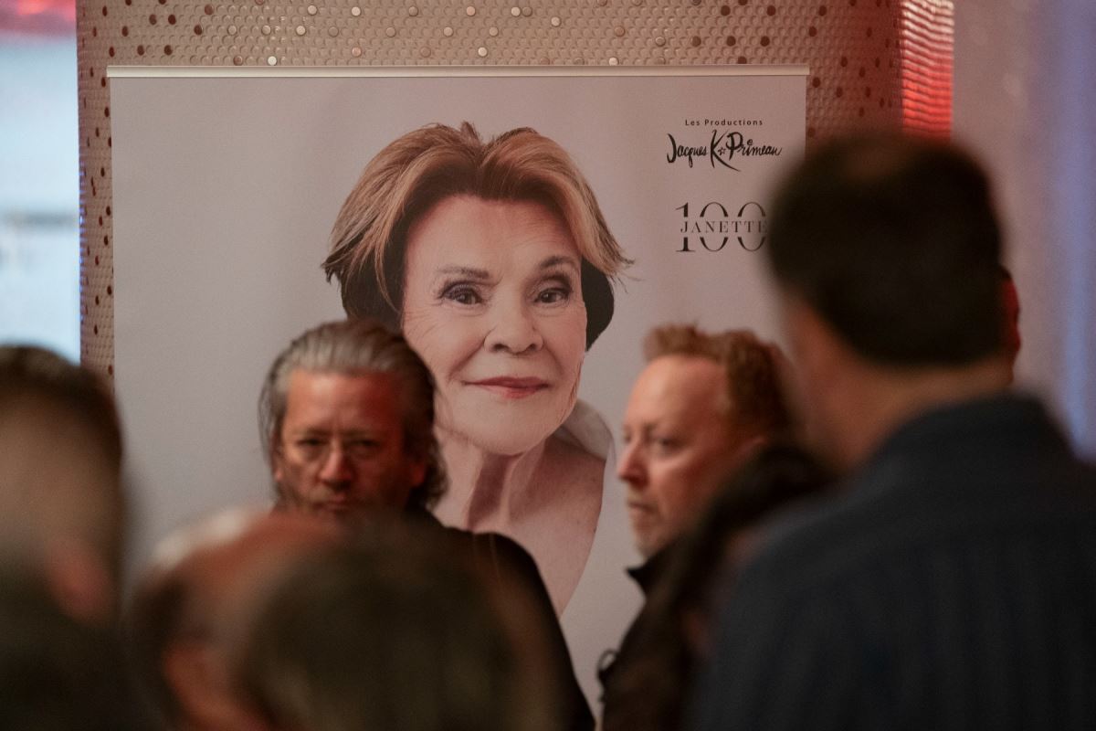 Une petite foule devant une affiche montrant Janette Bertrand et l'inscription Janette 100.