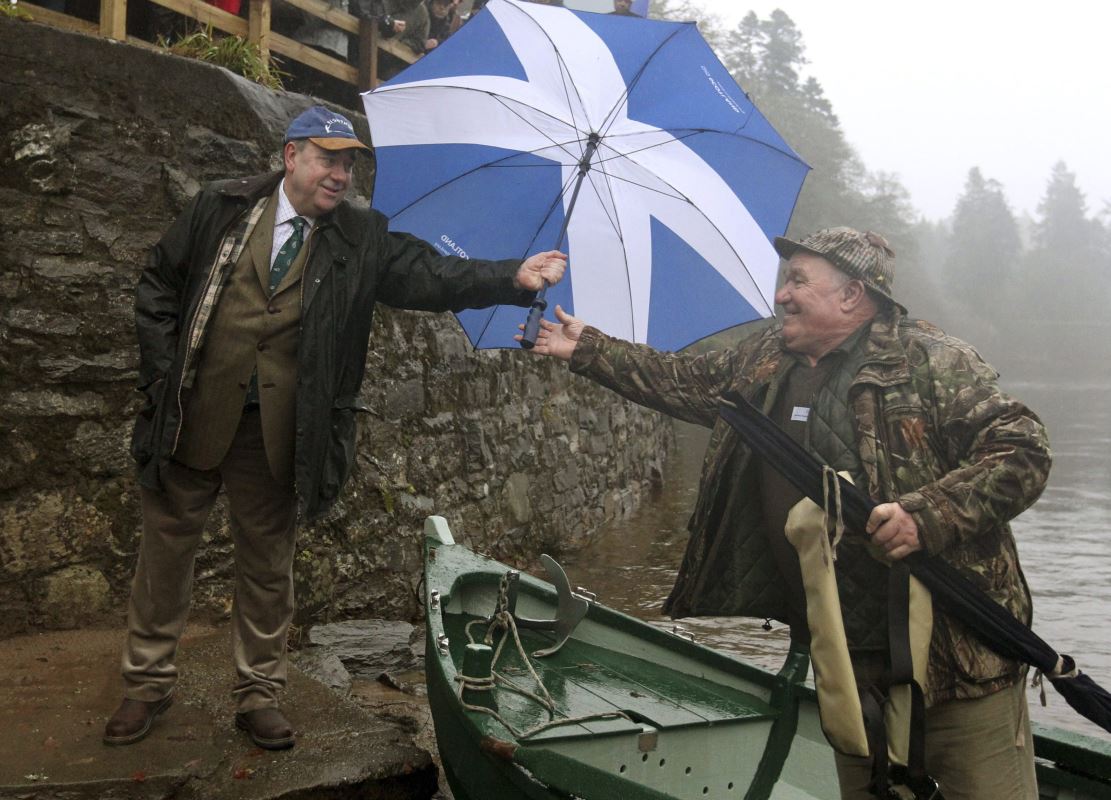 Le premier ministre d'Écosse Alex Salmond, à gauche, tend un parapluie à un pêcheur.