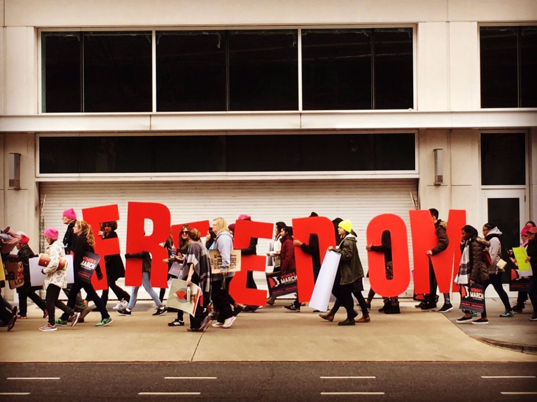 Des gens marchent en tenant des lettres de l'alphabet qui forment le mot « freedom » (« liberté » en français).