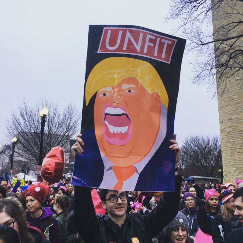 Un homme tient une pancarte avec une caricature de Donald Trump.