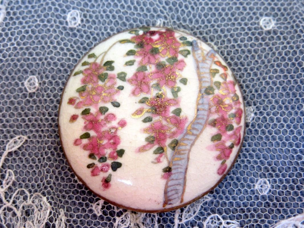 Bouton du début du 20e siècle fait en porcelaine et peint à la main. Le bouton est blanc et est décoré de fleurs roses.