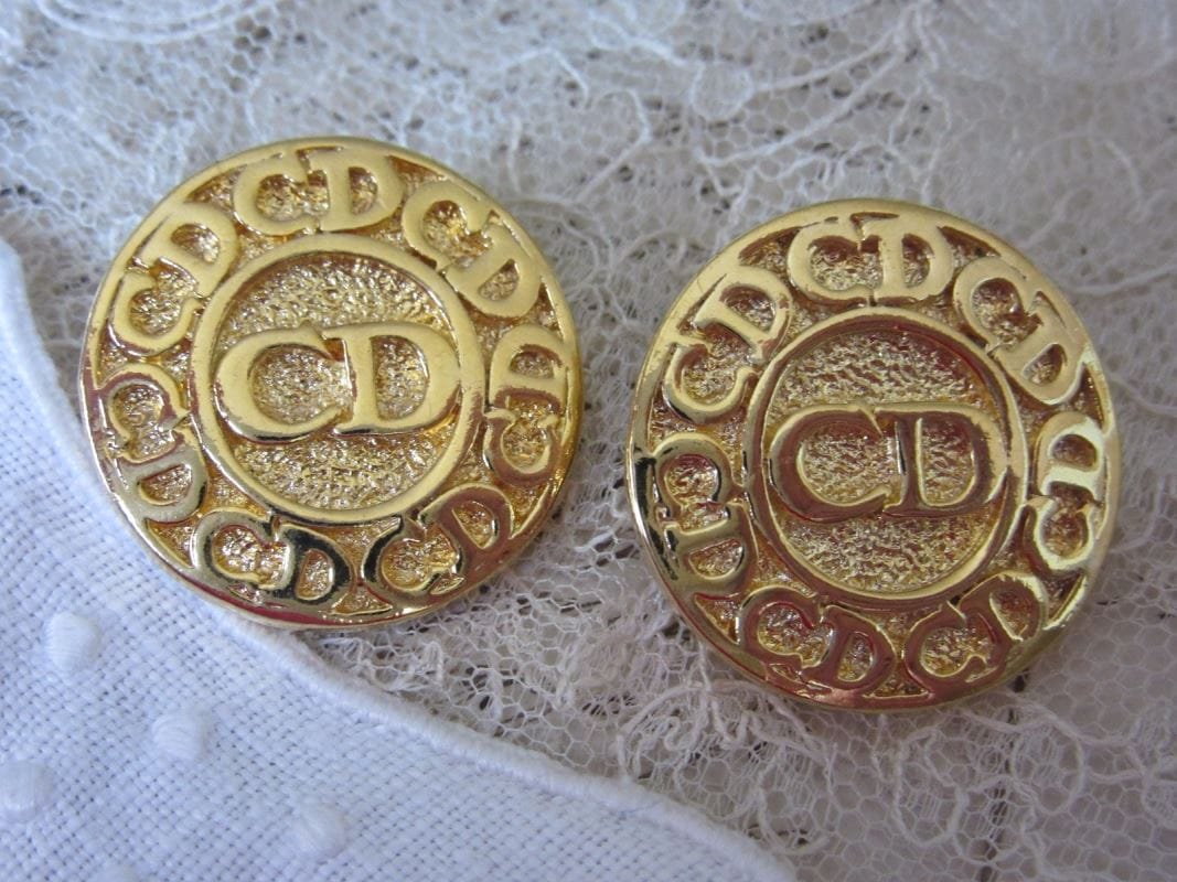 Une paire de boutons modernes de couleur dorée portant les initiales CD pour Christian Dior.